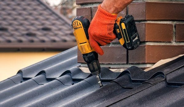 a professional roofer with electric screwdriver installs the roof near the chimney in Vaughan